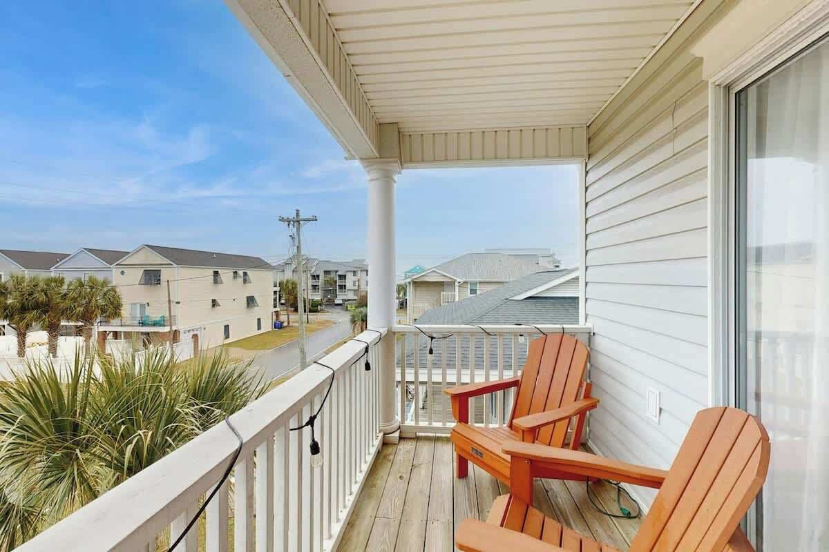 A balcony with two wooden chairs, a railing, and a view of neighboring houses.