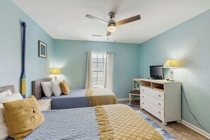 A bedroom with two beds, a ceiling fan, a TV on a dresser, and a window with curtains. - Hawleywood Beach Retreat (Surfside Beach)