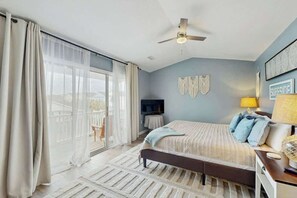 A bedroom with a bed, a ceiling fan, a TV, a lamp, and a view of the outdoors. - Hawleywood Beach Retreat (Surfside Beach)