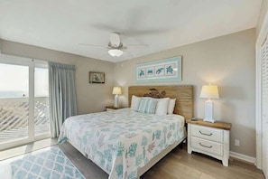 A bedroom with a bed, two bedside tables, a ceiling fan, and a view of the outdoors. - Shore Breeze Unit 2 Condo (North Myrtle Beach)