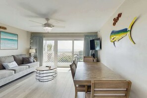 Un salon moderne avec un canapé, une table basse, une table à manger et un ventilateur de plafond. On y trouve un téléviseur posé sur un meuble et un poisson décoratif accroché au mur.