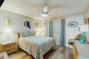 Une chambre à coucher comprenant un lit, une table de chevet, une chaise, une table, un ventilateur de plafond et des éléments de décoration murale.