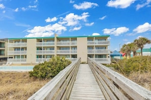 A multi-story hotel with balconies, a pool, and a wooden walkway leading to the entrance. - Shore Breeze Unit 2 Condo (North Myrtle Beach)