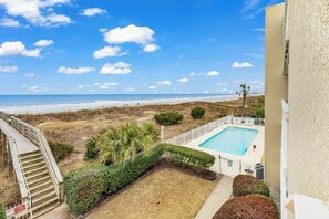 A pool area with a view of the beach, a wooden staircase, and a fenced pool. - Shore Breeze Unit 2 Condo (North Myrtle Beach)