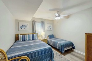 A bedroom with two beds, a ceiling fan, and artwork on the walls. - Shore Breeze Unit 2 Condo (North Myrtle Beach)