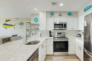 A modern kitchen with white cabinets, stainless steel appliances, and decorative fish wall art. - Shore Breeze Unit 2 Condo (North Myrtle Beach)