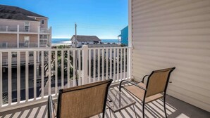 A balcony with two chairs, a view of the beach, and buildings in the background. - Coconut Grove Unit 203 (North Myrtle Beach)