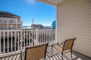A balcony with two chairs, a view of the beach, and buildings in the background. - Coconut Grove Unit 203 (North Myrtle Beach)