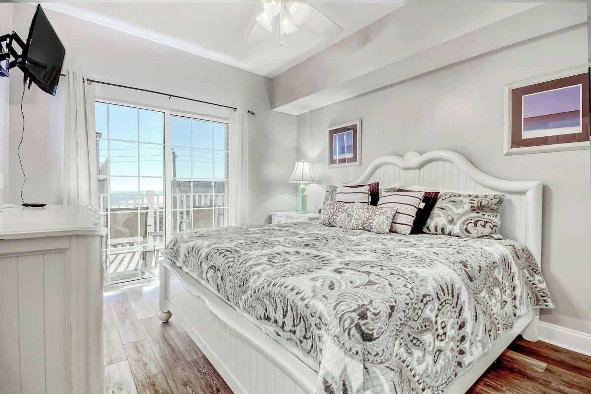 A bedroom with a bed, a nightstand, a lamp, a TV, and a window with a view.