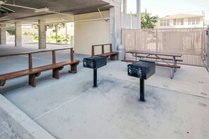 Een terras met banken en tafels, een prullenbak en een hek.