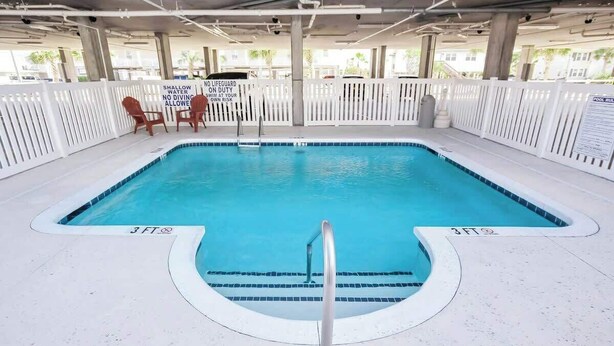 A 3-foot deep shallow pool with a lifeguard sign, white deck, and a fence. - Coconut Grove Unit 203 (North Myrtle Beach)