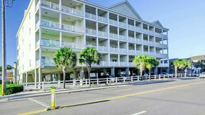 A multi-story hotel with balconies, a parking area, and palm trees. - Coconut Grove Unit 203 (North Myrtle Beach)