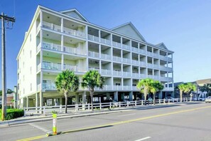 A multi-story hotel with balconies, a parking area, and palm trees. - Coconut Grove Unit 203 (North Myrtle Beach)