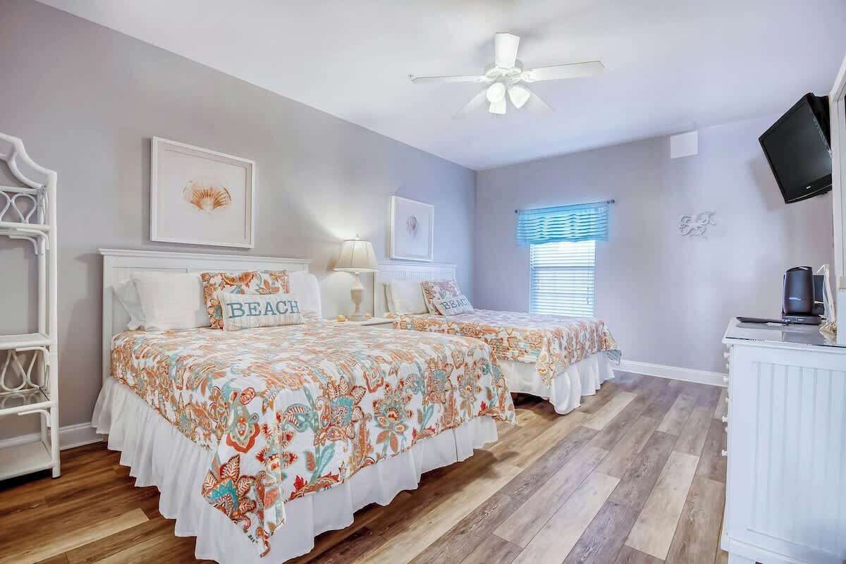 A bedroom with two beds, a ceiling fan, a television, and a window with blinds.
