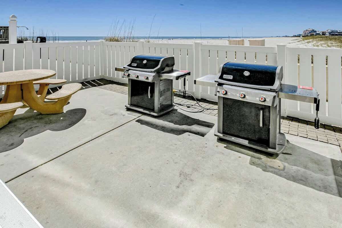 Une terrasse extérieure avec deux barbecues, une table jaune et une clôture blanche.