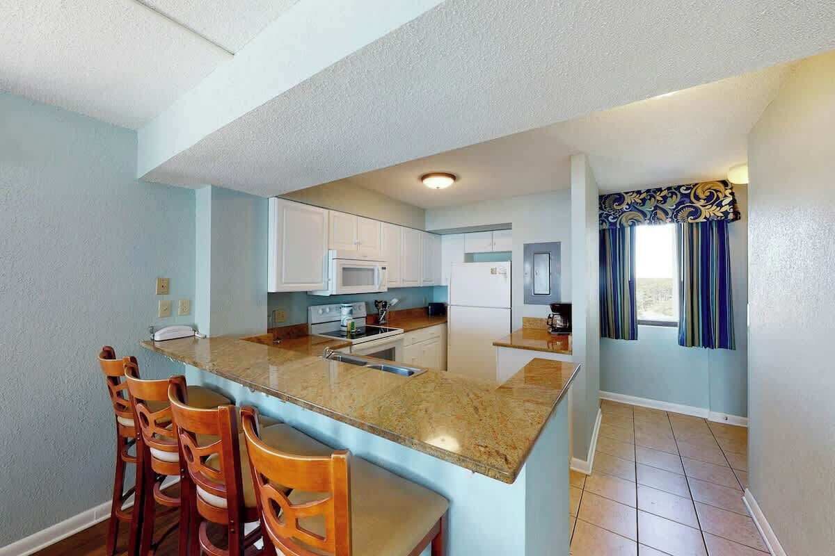 A kitchen with a central island, wooden chairs, and a window with curtains.