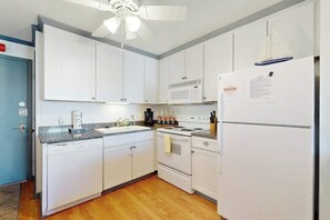 A kitchen with white cabinets, a microwave, a stove, and a refrigerator. - Beach Cottages at OD - 33B (North Myrtle Beach)