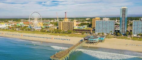 A coastal cityscape with a pier extending into the water, a large Ferris wheel, and modern buildings.