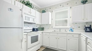 A kitchen with white cabinetry, a microwave, a stove, and a window with blinds. - The Havens Unit 1721 (North Myrtle Beach)