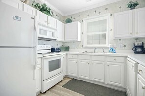 A kitchen with white cabinetry, a microwave, a stove, and a window with blinds. - The Havens Unit 1721 (North Myrtle Beach)