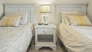 A bedroom with two beds, each with a white headboard, a bedside table with a lamp, and a drawer. - The Havens Unit 1721 (North Myrtle Beach)