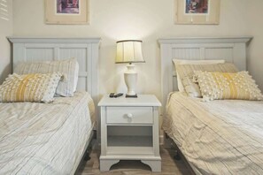 A bedroom with two beds, each with a white headboard, a bedside table with a lamp, and a drawer. - The Havens Unit 1721 (North Myrtle Beach)