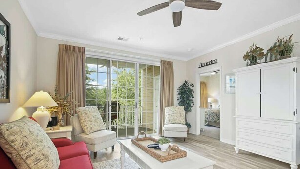 A living room with a red sofa, white armchairs, a coffee table, a ceiling fan, and a white cabinet. - The Havens Unit 1721 (North Myrtle Beach)