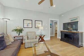 A living room with a sofa, armchair, coffee table, TV stand, and artwork on the wall. - Cinzia Lane Bungalow (North Myrtle Beach)
