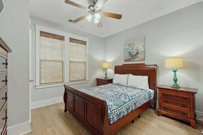 A bedroom with a wooden bed, two bedside tables with lamps, a ceiling fan, and a window with blinds. - Cinzia Lane Bungalow (North Myrtle Beach)