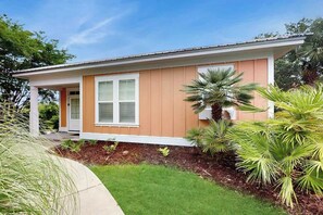 A single-story house with a front porch, a window, and a small garden with palm trees. - Cinzia Lane Bungalow (North Myrtle Beach)
