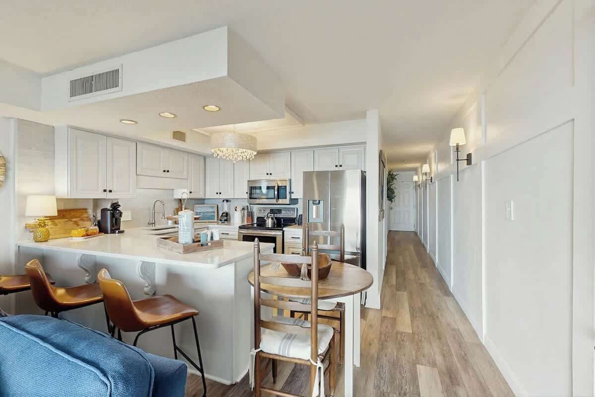 Una cocina moderna con armarios blancos, una isla central y un comedor con sillas.