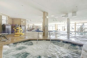 An indoor swimming pool with a central water feature, surrounded by a spacious area with large windows and a staircase. - Madiera Magic Retreat (North Myrtle Beach)