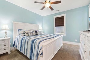 Ein Schlafzimmer mit einem Bett, einem Deckenventilator, einem Fenster mit Jalousien und einem Schminktisch.