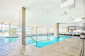 An indoor swimming pool with clear glass walls, a concrete floor, and a few lounge chairs. - Madiera Magic Retreat (North Myrtle Beach)