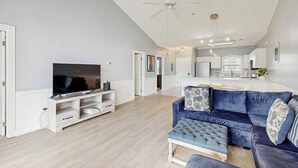 A living room with a television, a blue sofa, and a ceiling fan. - Carnation Unit 302 Condo (Myrtle Beach)