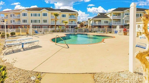 A residential building with a swimming pool, outdoor seating, and a fenced area. - Carnation Unit 302 Condo (Myrtle Beach)