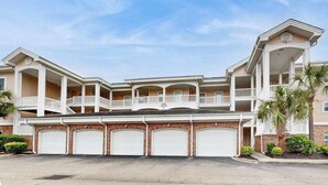 A multi-story residential building with a central balcony, multiple garage doors, and a symmetrical facade. - Carnation Unit 302 Condo (Myrtle Beach)