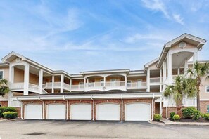 A multi-story residential building with a central balcony, multiple garage doors, and a symmetrical facade. - Carnation Unit 302 Condo (Myrtle Beach)