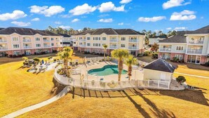 A multi-story hotel with a swimming pool, outdoor seating, and a fenced patio area. - Carnation Unit 302 Condo (Myrtle Beach)