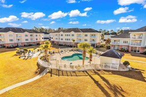 A multi-story hotel with a swimming pool, outdoor seating, and a fenced patio area. - Carnation Unit 302 Condo (Myrtle Beach)