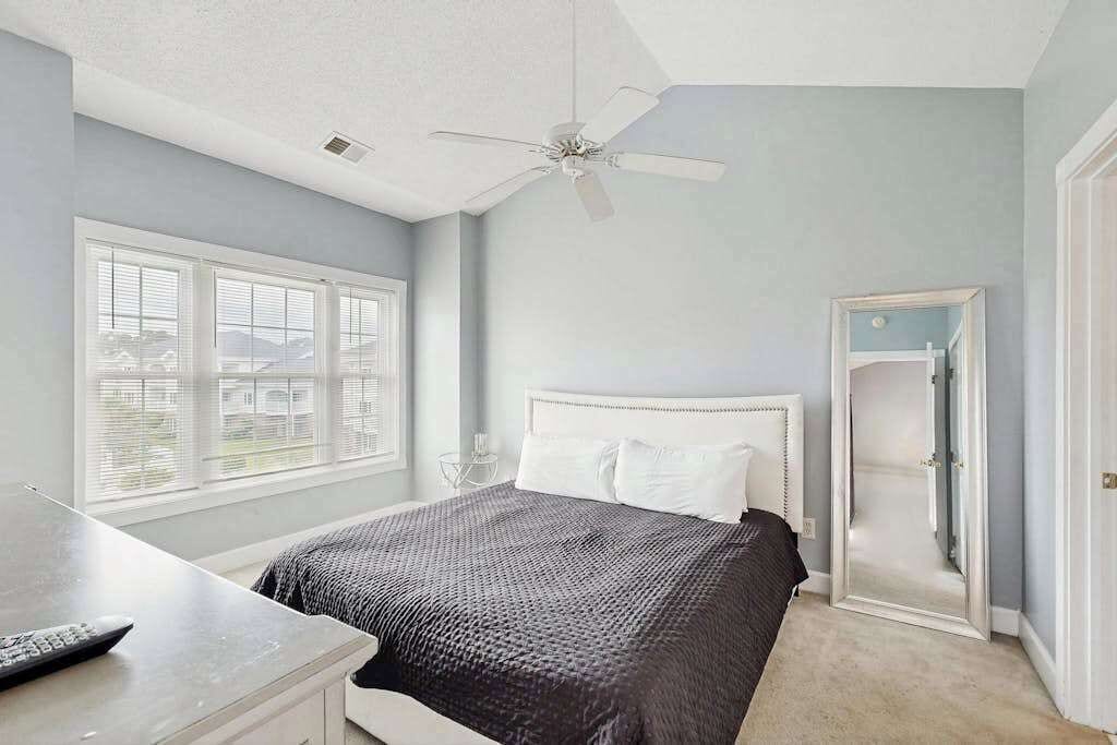 A bedroom with a bed, a desk, a ceiling fan, and a window with blinds.