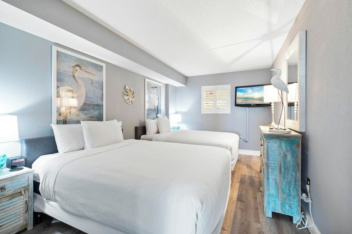 Une chambre d’hôtel avec deux lits, une télévision, des œuvres d’art accrochées aux murs et une commode.
