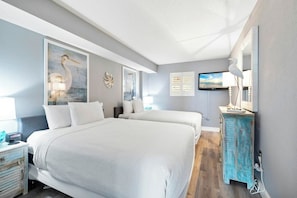 A hotel room with two beds, a television, artwork on the walls, and a dresser.