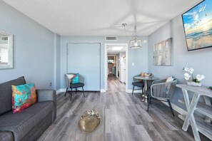 A living room with a sofa, chairs, a coffee table, and a dining table. There is a hallway leading to another room. - Bay Watch Resort 0439 (North Myrtle Beach)