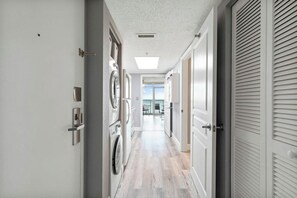 A laundry room with a washing machine, dryer, and a door leading to a hallway. - Bay Watch Resort 0439 (North Myrtle Beach)