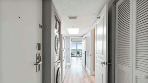 A hallway with a washing machine, a door with a handle, and a ceiling vent. - Bay Watch Resort 0439 (North Myrtle Beach)