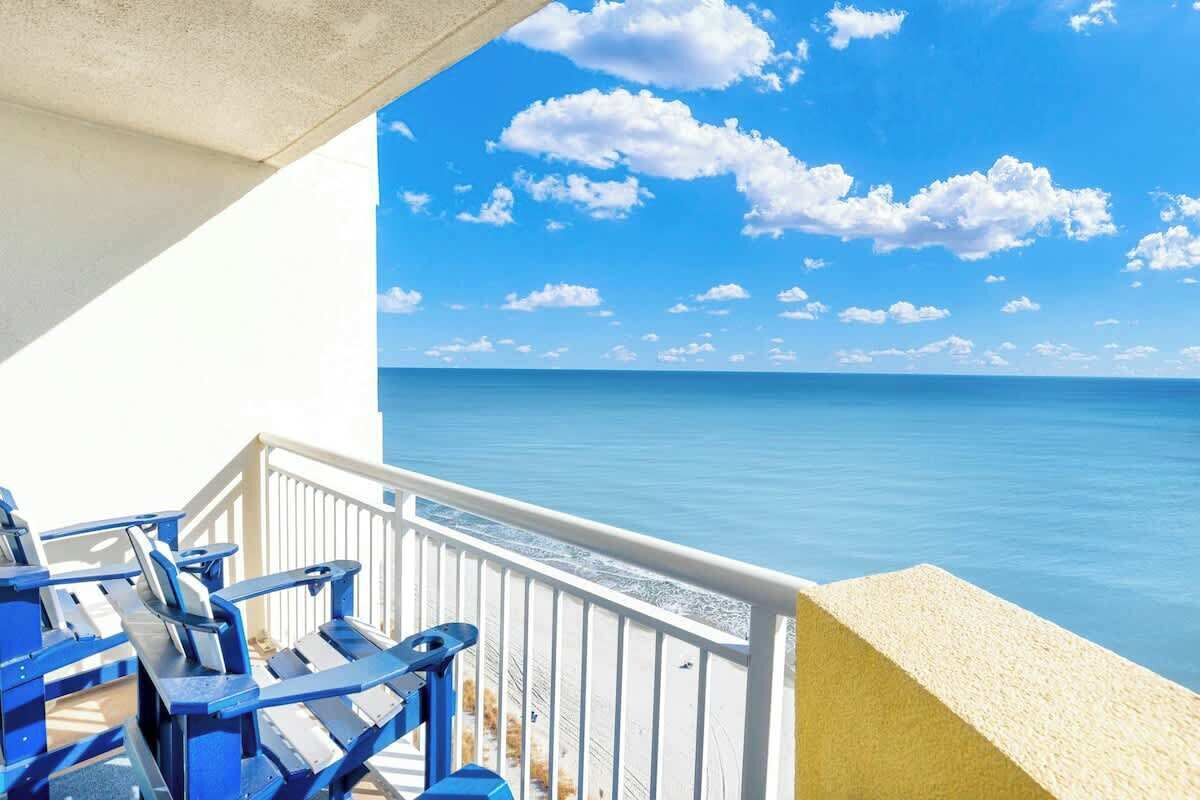 Ein Balkon mit blauen Stühlen mit Blick auf ein klares, blaues Meer unter einem strahlend blauen Himmel.