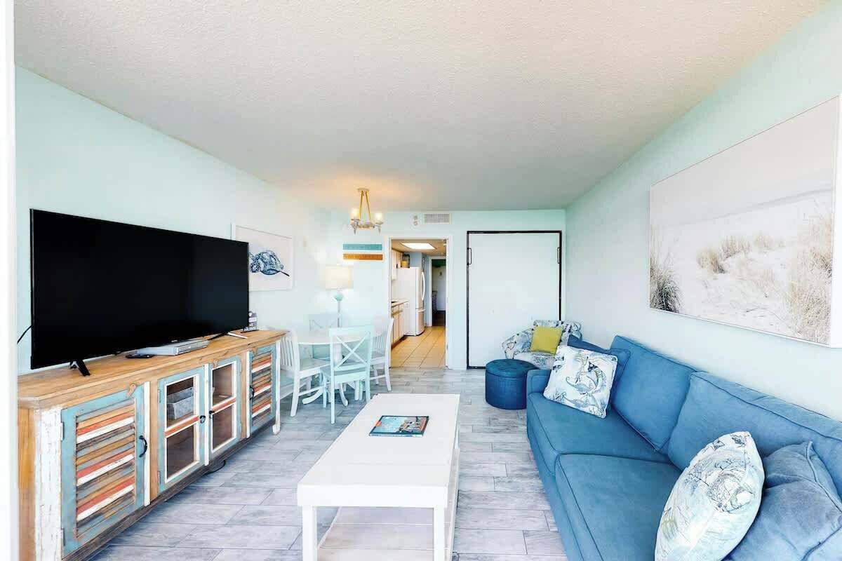 A living room with a television, a sofa, a coffee table, and a dining area with chairs.