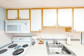A kitchen with white cabinets, a microwave, a stove, a coffee maker, and a sink. - Bay Watch Resort 1803 (North Myrtle Beach)