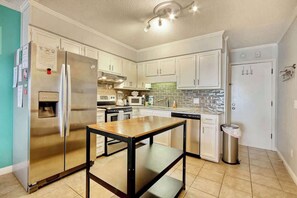 A kitchen with white cabinets, a stainless steel refrigerator, a microwave, and a dishwasher. - Cherry Grove Retreat (North Myrtle Beach)